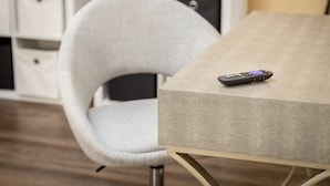 Quarto moderno com uma poltrona clara, mesa com textura e controle remoto sobre a mesa.