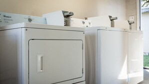 Duas máquinas de lavar roupa Whirlpool de abertura frontal numa lavanderia com janela.