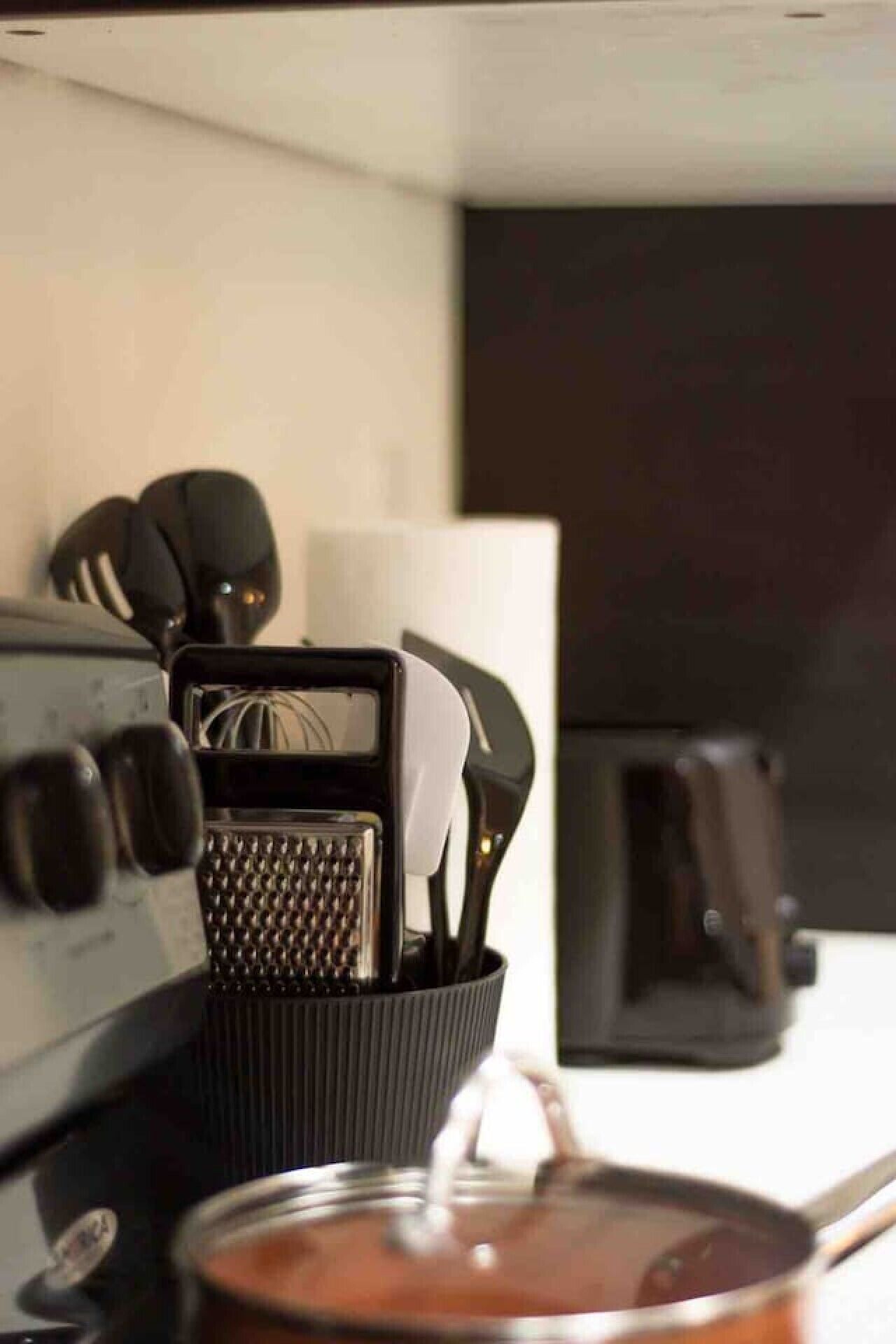 A kitchen counter with a grater, whisk, and utensils in a holder, a toaster, and a pot with a spoon.