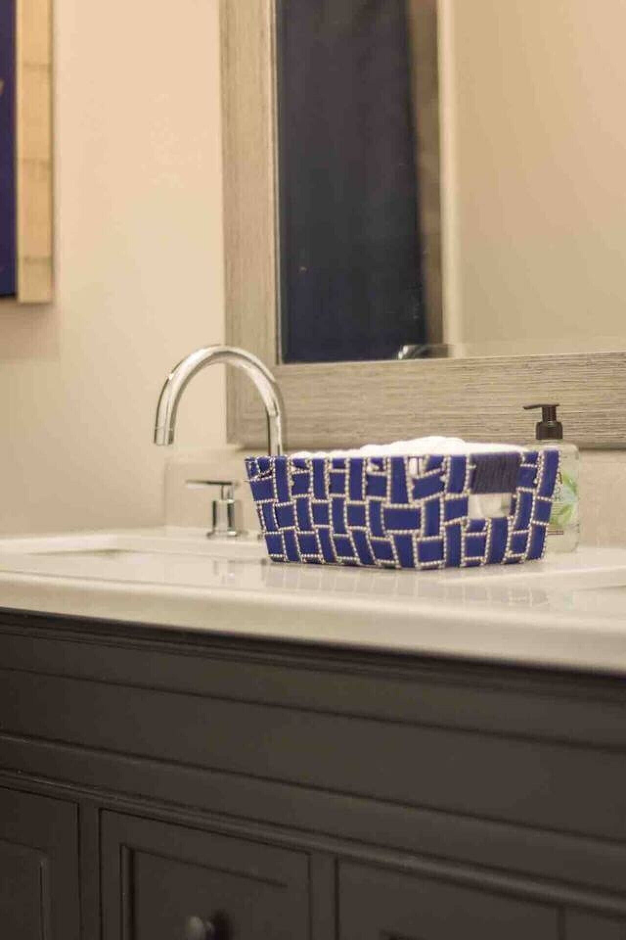 A bathroom with a white sink, a mirror above it, and a blue patterned basket on the sink.