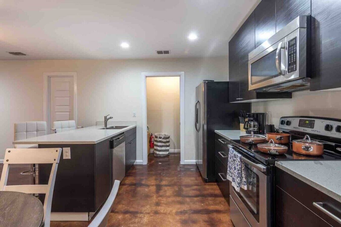 A compact kitchen with a dishwasher, stove, microwave, and a small dining area with a chair and table.