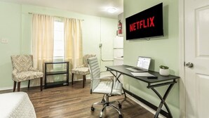 A hotel room with a bed, two chairs, a desk with a laptop, a TV mounted on the wall, and a window with curtains. - Central Junior Suite Fast-WiFi  First Floor (McAllen)