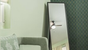 A room with a large mirror, a ceiling fan, a patterned wall, and a sofa with a cushion. - Central Junior Suite Fast-WiFi  First Floor (McAllen)