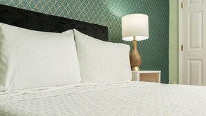 A neatly made bed with white bedding, a wooden nightstand with a lamp, and a patterned wall. - Central Junior Suite Fast-WiFi  First Floor (McAllen)