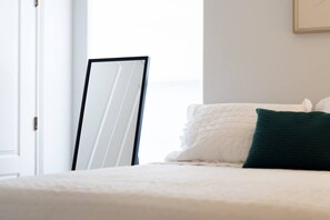 A bed with white bedding and a green pillow, a white door, and a framed mirror leaning against the wall.