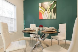 A dining area with a glass table, white chairs, and a teal accent wall.