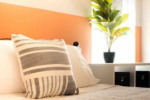 A bed with striped pillows, a potted plant, and a window with blinds.