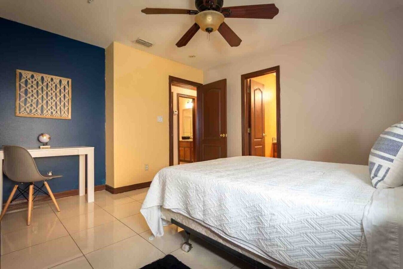 Ein Schlafzimmer mit einem Bett, einem Schreibtisch, einem Sessel, einem Deckenventilator und zwei Türen.