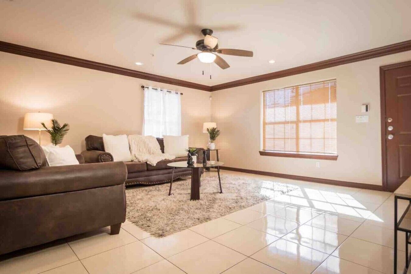 A living room with a brown sofa, a coffee table, a ceiling fan, and a large window with blinds.