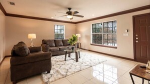 A spacious living room with a ceiling fan, a brown leather sofa, a glass coffee table, and a large window. - Fast Wi-Fi Spacious & Cozy Central DT Home (McAllen)