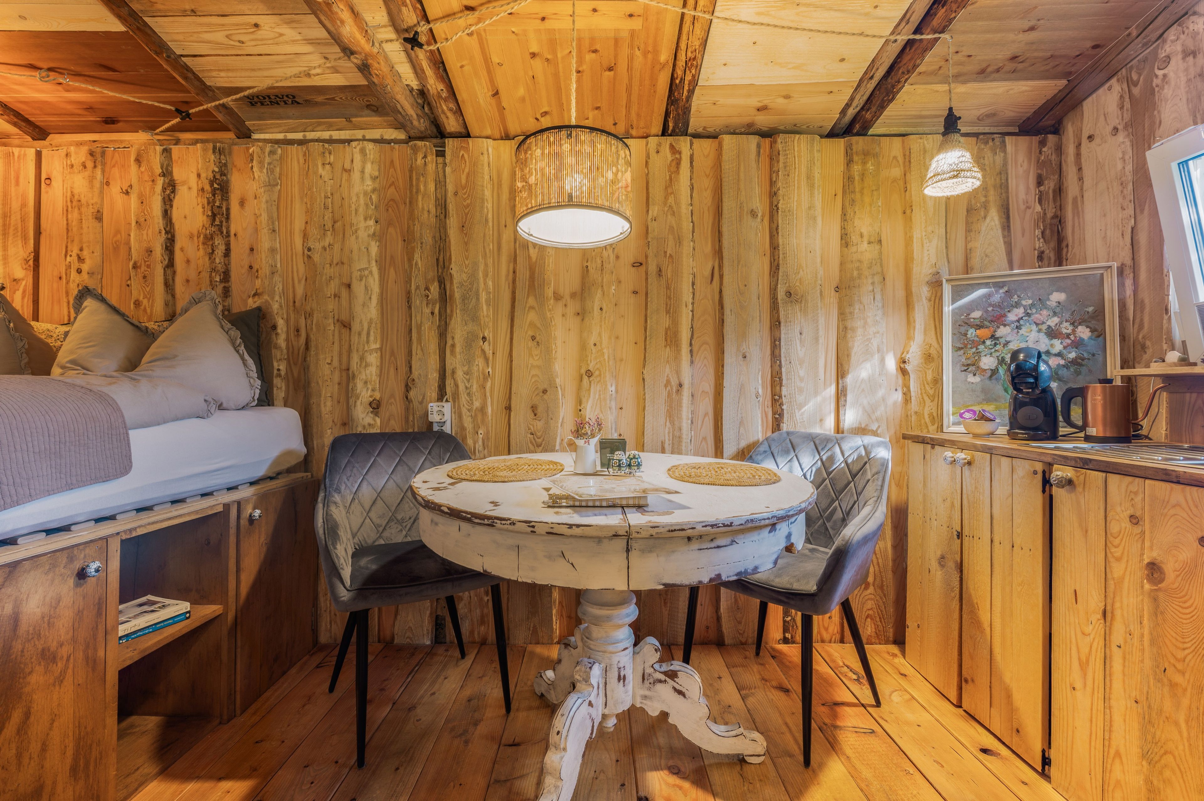 Interior acogedor de una cabaña con una cama, una mesa de comedor redonda y una estación de café.