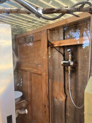 A wooden bathroom with a shower, a toilet, and a metal roof structure.
