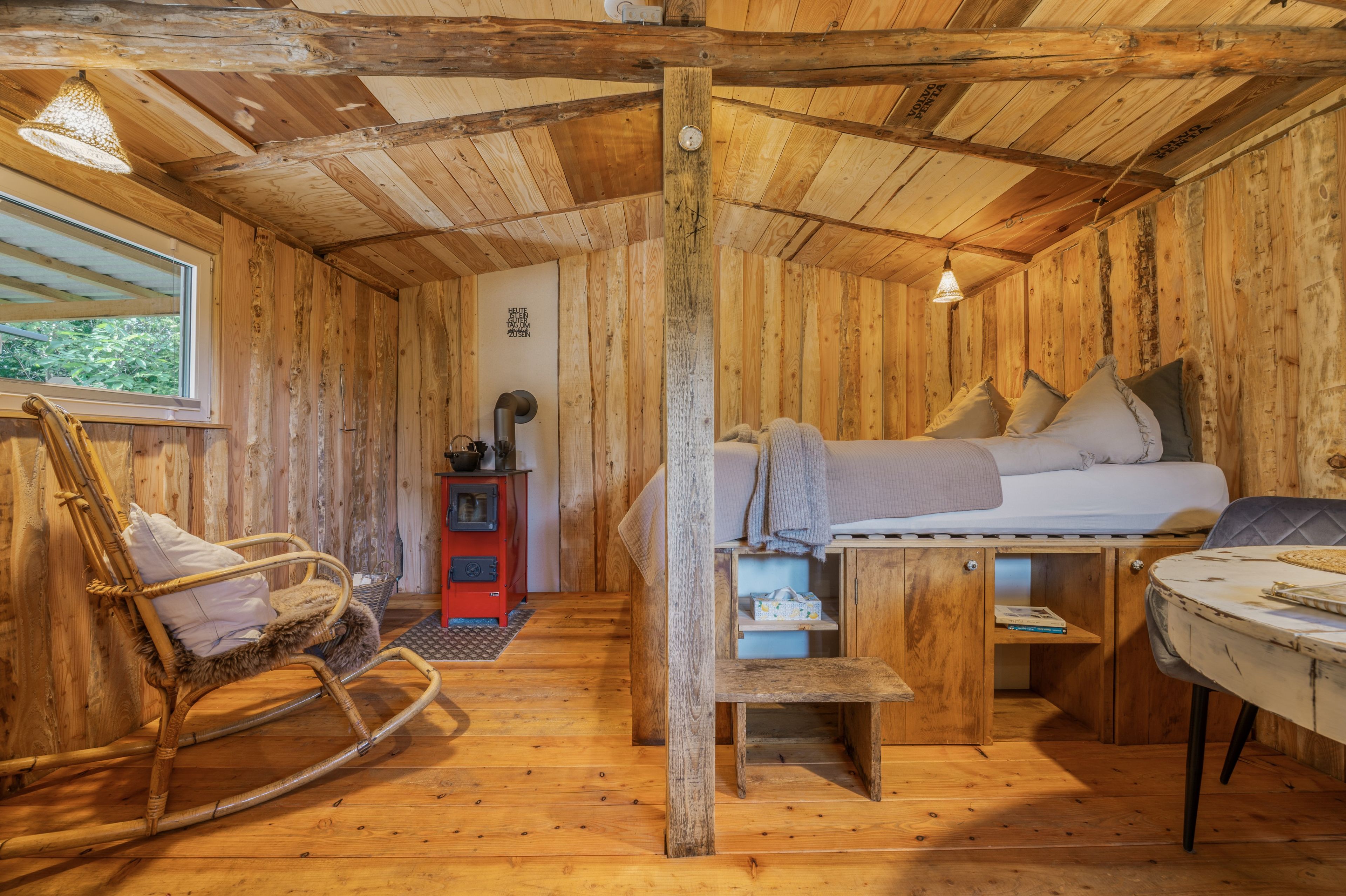 Ein gemütliches Blockhaus-Interieur mit einem Bett, einem Schaukelstuhl, einem kleinen Tisch und einem Herd.