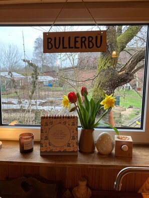 Una ventana con un cartel que dice 'BULLERBU', un cuaderno, una vela y un florero con flores.