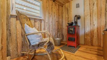 Un interior de madera con una mecedora, una estufa roja y una ventana con persianas.