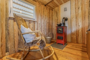 A wooden interior with a rocking chair, a red stove, and a window with blinds. - Holiday Home 'Glamping Cottage with Hot Tub' with Private Pool, Private Terrace and Wi-Fi (Hipstedt)