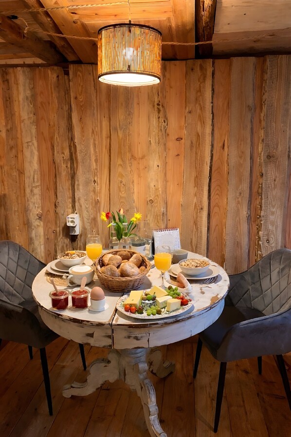 A wooden interior with a round table set for breakfast, including bread, cheese, and fruit.