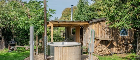 A hot tub surrounded by a wooden deck, with a small shed and a barbecue grill in the background.