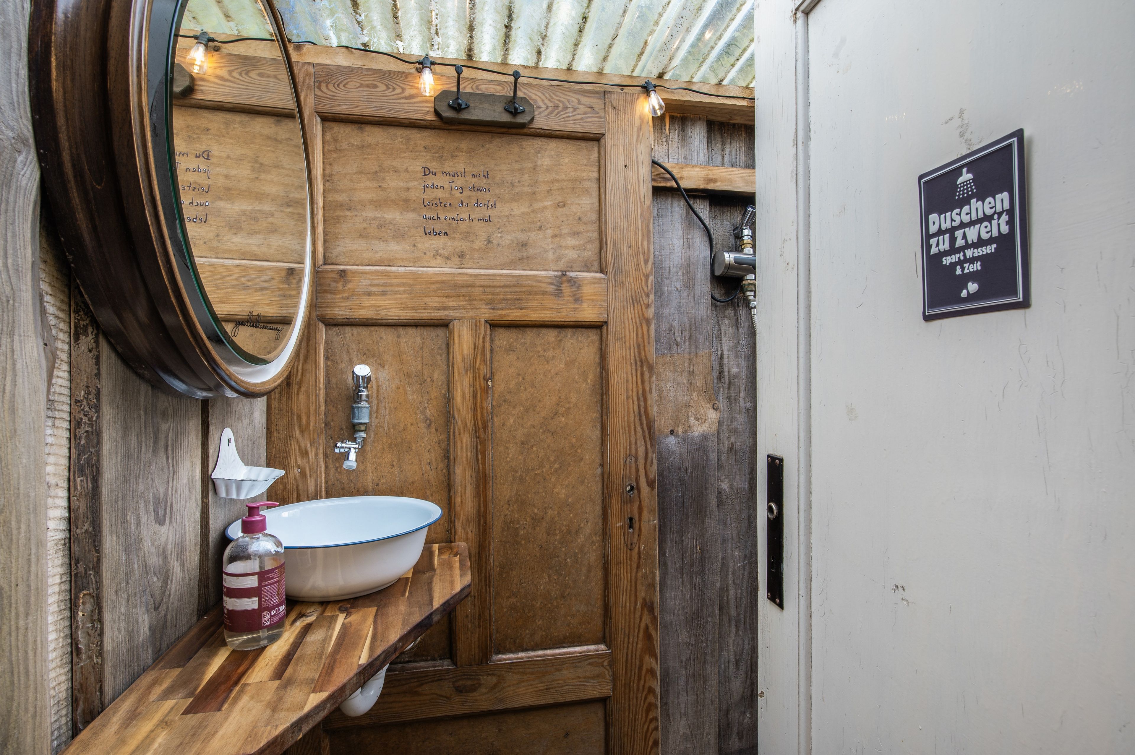 A rustic wooden bathroom with a white sink, a mirror, and a sign indicating water and time availability.