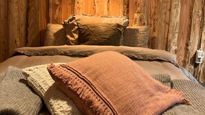 Interno di una baita in legno con un letto, cuscini e una lampada a sospensione.