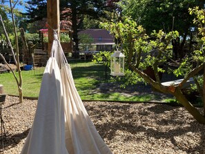A hammock in a garden with a house and trees in the background.