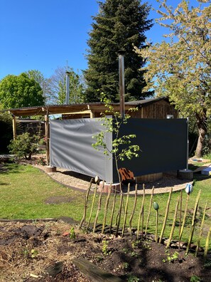 Un jardín con una estructura cubierta, una valla de madera y un edificio al fondo.