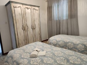 A room with two beds, a wardrobe, and a window with curtains. - Casa Rural Villagarcia – Comfort and Privacy in El Real de la Jara (El Real de la Jara)