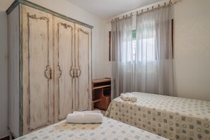 A room with two beds, a wardrobe, a small wooden shelf, and a window with curtains. - Casa Rural Villagarcia – Comfort and Privacy in El Real de la Jara (El Real de la Jara)