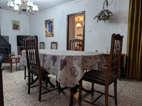 A dining room with a table set for four, surrounded by wooden chairs. There is a chandelier above the table, a painting on the wall, and a door leading to another room.. Casa Rural Villagarcia – Comfort and Privacy in El Real de la Jara