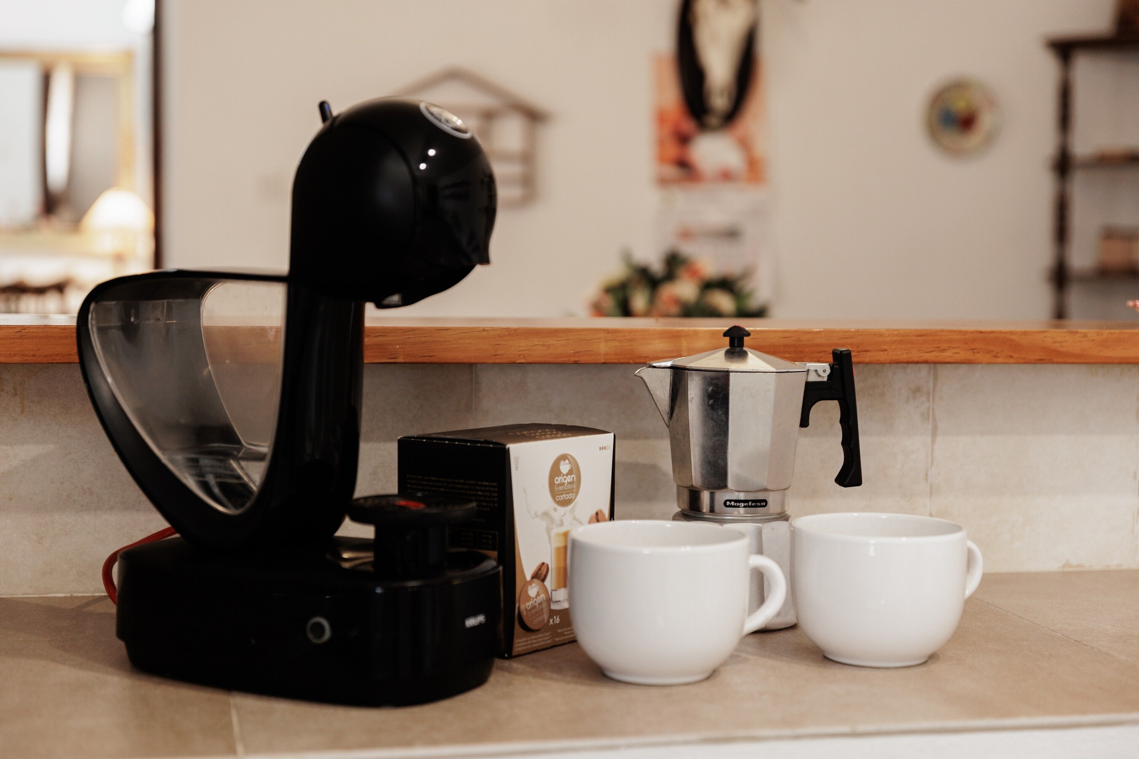 Une machine à café, deux tasses blanches et une boîte sur un plan de travail de cuisine.