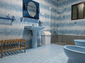 Une salle de bain équipée d’un lavabo, d’un miroir, d’une douche et d’un banc en bois.