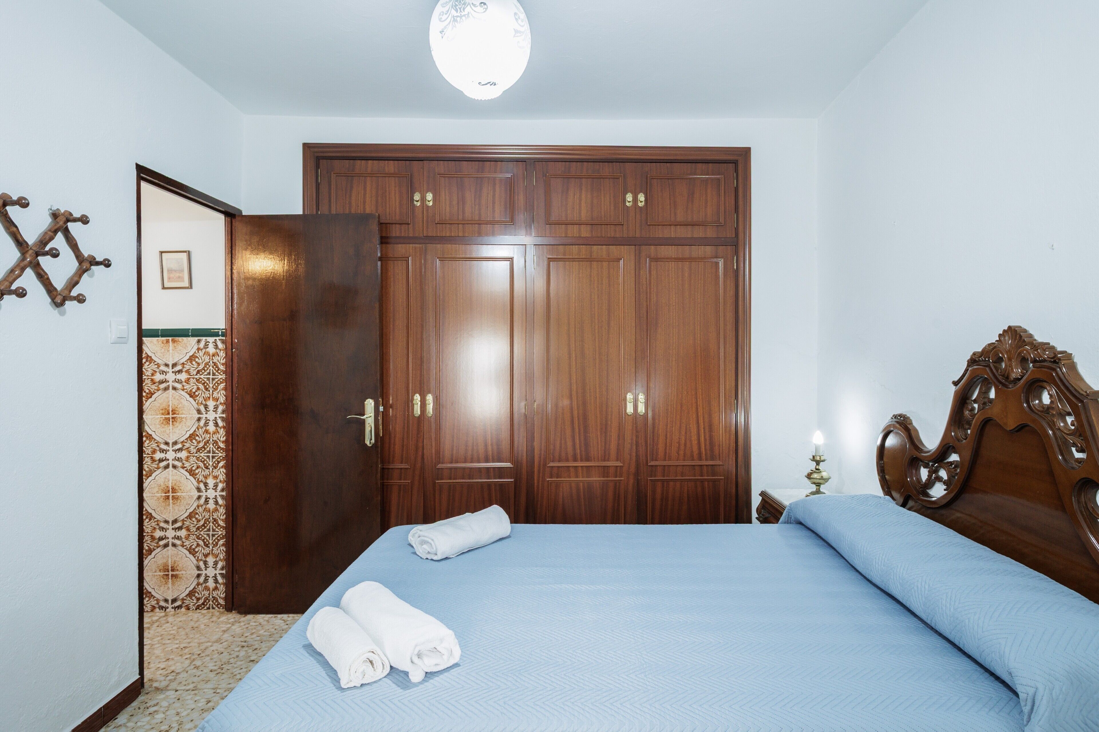 Un dormitorio con cama, un armario de madera y una lámpara fijada a la pared.