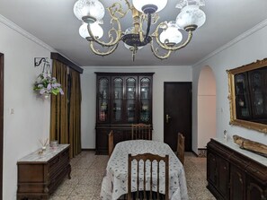 Une salle à manger avec un lustre, un buffet aux portes vitrées, une table recouverte d’une nappe à motifs et un miroir au mur.