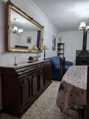 Ein Zimmer mit einem großen, verzierten Spiegel, einem Holzschrank, einem blauen Sofa, einem Tisch mit gemustertem Tuch und einer Kandelaber.