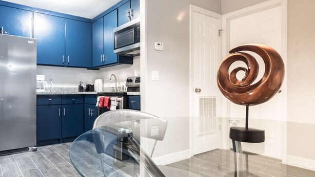 A modern kitchen with blue cabinets, stainless steel appliances, and a glass dining table. - ✅ RARE FIND! KING  Size Bed Central Mcallen WiFi ✅ (McAllen)
