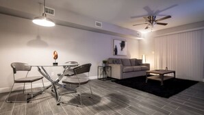 A modern living room with a glass dining table, metal chairs, a sofa, a coffee table, a ceiling fan, and a black rug. - ✅ RARE FIND! KING  Size Bed Central Mcallen WiFi ✅ (McAllen)