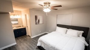 A bedroom with a bed, a ceiling fan, a window with blinds, and a bathroom with a sink and mirror. - ✅ RARE FIND! KING  Size Bed Central Mcallen WiFi ✅ (McAllen)