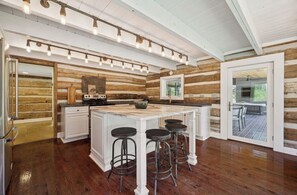 Una cocina con una isla grande, taburetes de bar, paredes de madera y vistas a través de un ventanal.