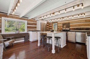Una cocina con paredes de madera, un ventanal grande, taburetes de bar y una isla central.
