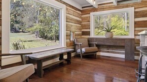 Ein rustikales Blockhaus-Interieur mit Holzwänden, großen Fenstern, einer Bank und einem Sessel.