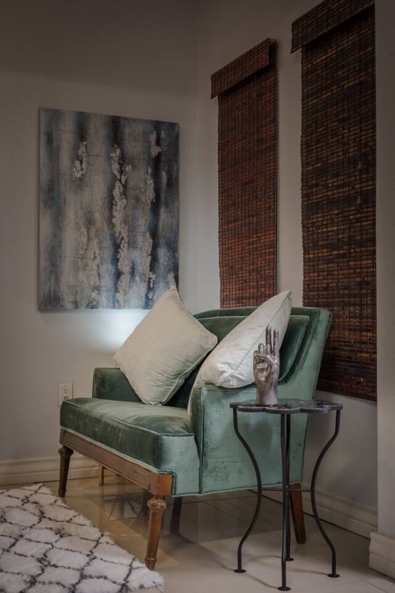 A green sofa with wooden legs, a white pillow, and a metal side table with a glass top.