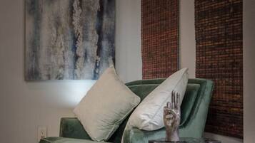 A green sofa with wooden legs, a white pillow, and a metal side table with a glass top.