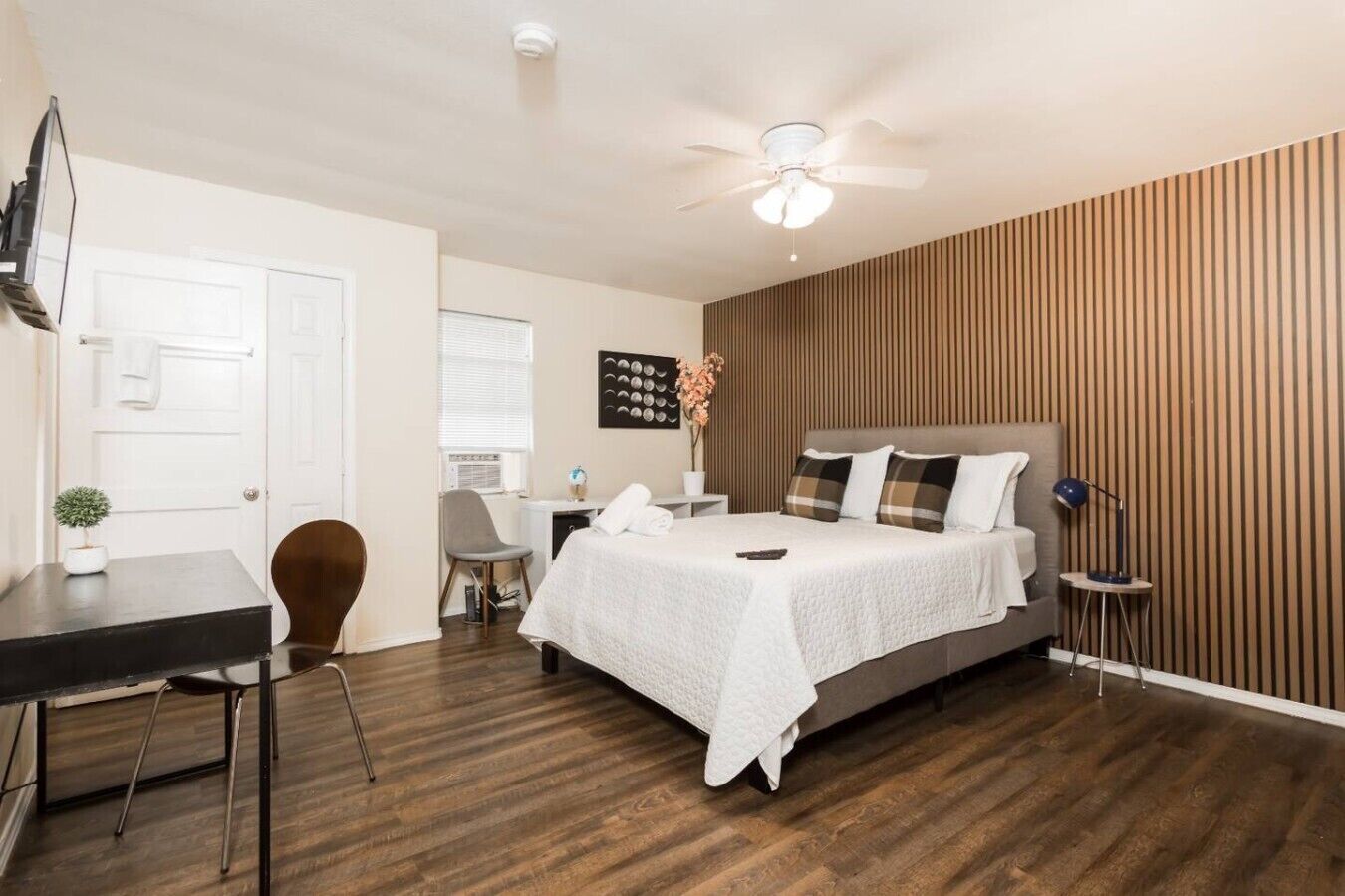 A bedroom with a bed, a desk, a chair, a ceiling fan, and a wall-mounted artwork.