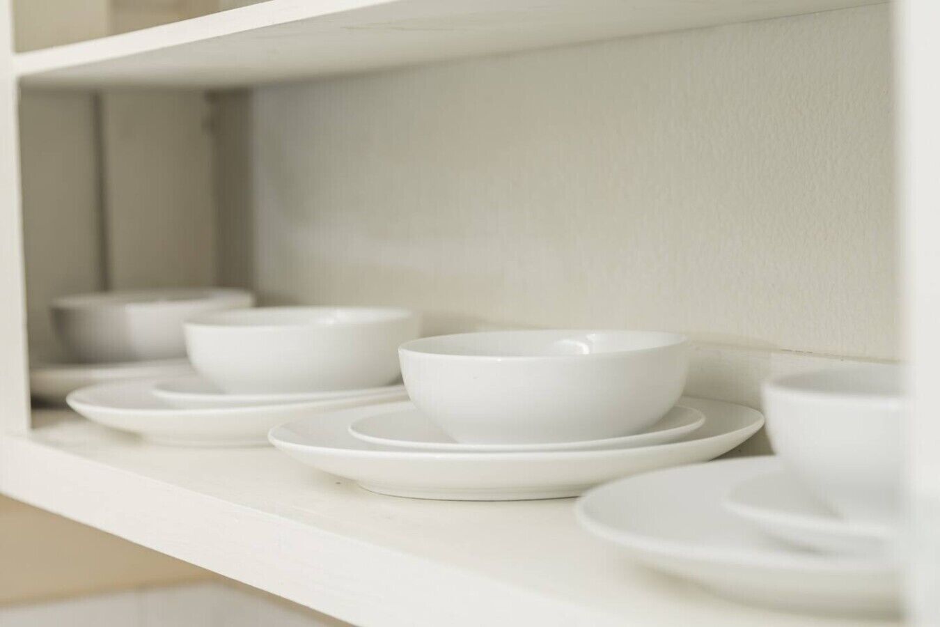 Une étagère blanche sur laquelle sont disposés plusieurs bols et assiettes blancs.