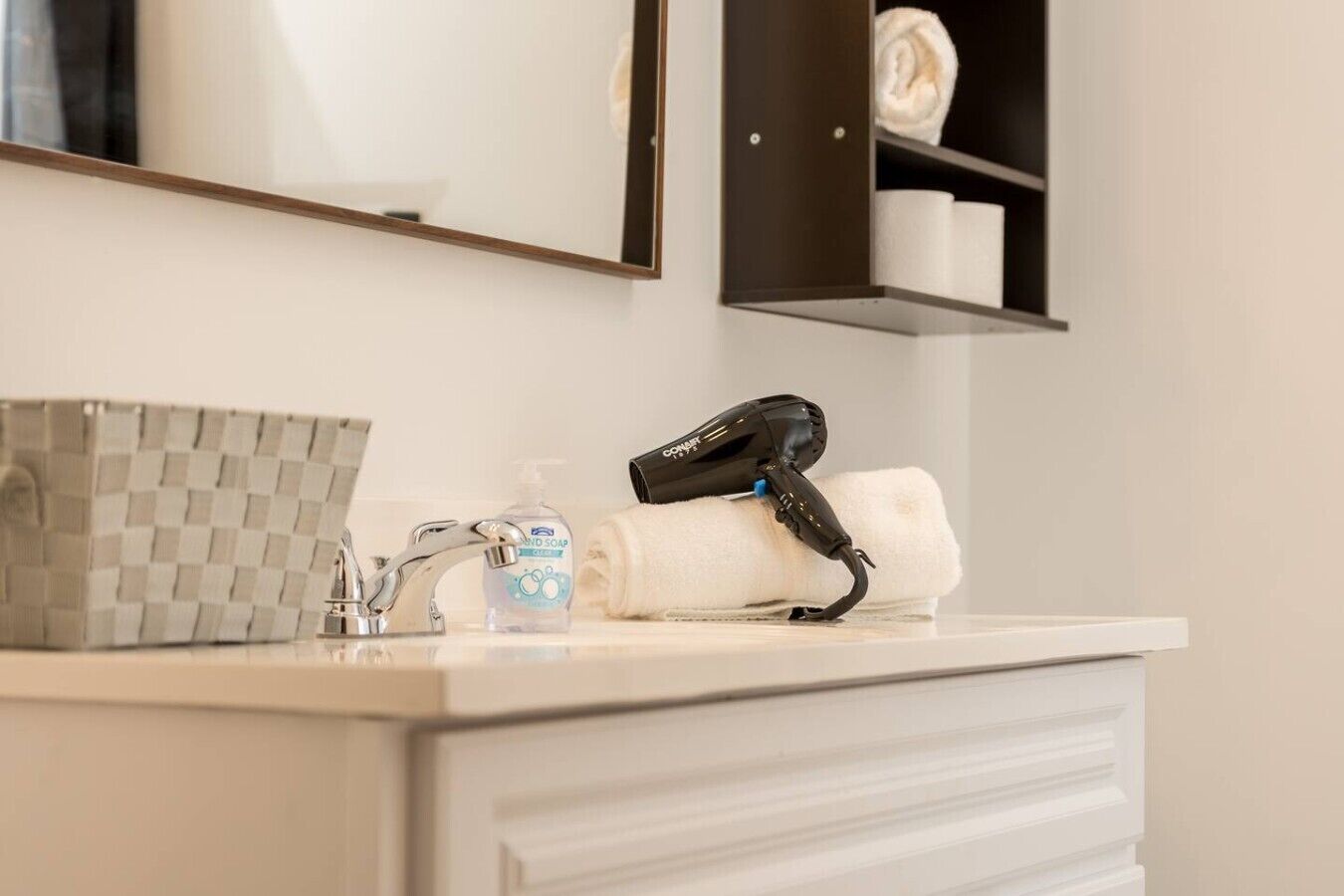A bathroom with a checkered soap dispenser, a hand soap bottle, a hairdryer, and a towel on the counter.