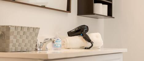 A bathroom with a checkered soap dispenser, a hand soap bottle, a hairdryer, and a towel on the counter.