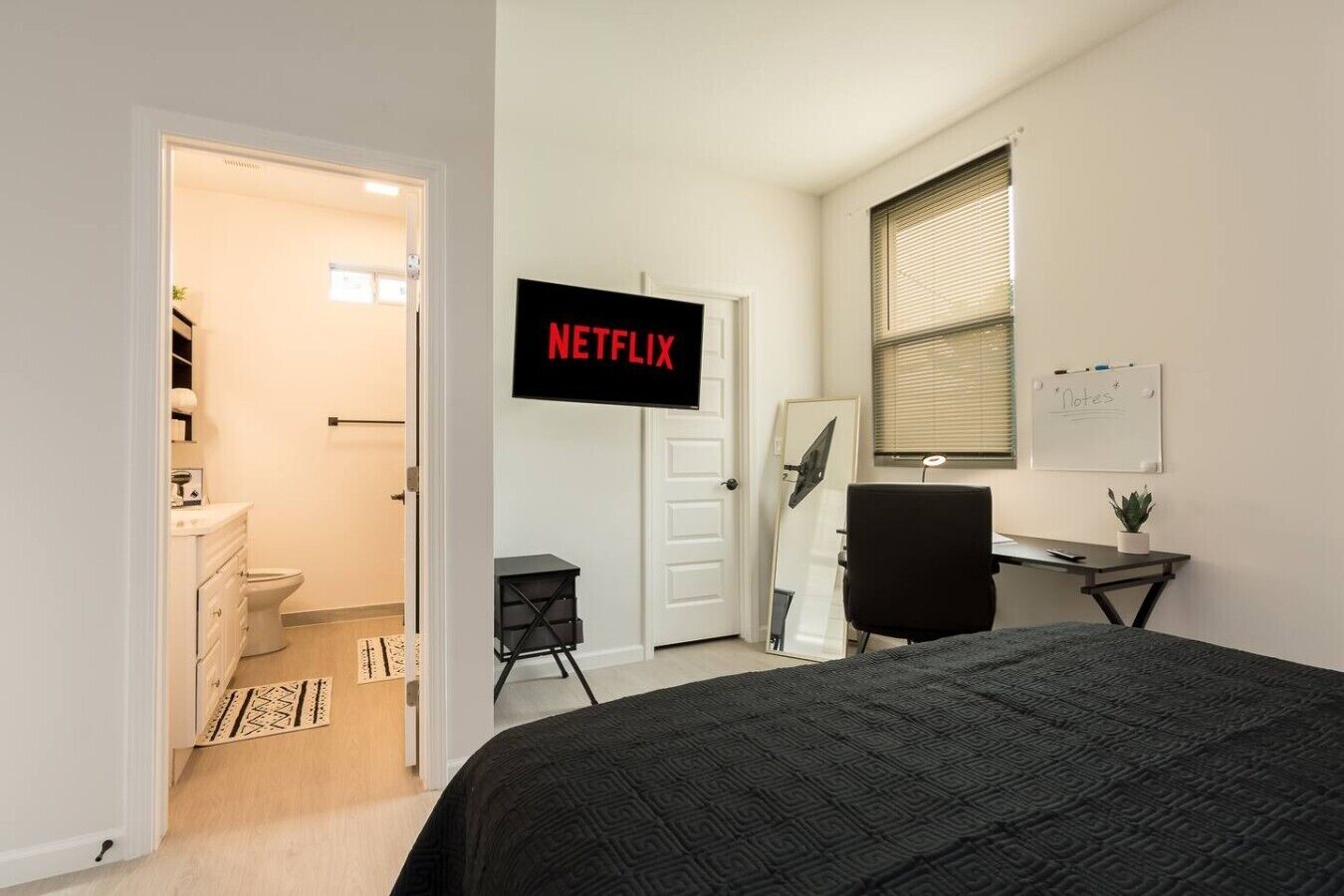A bedroom with a bed, a desk, a chair, a TV, a whiteboard, and a bathroom.