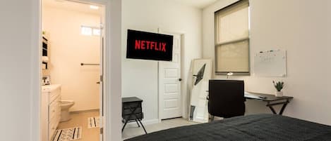 A bedroom with a bed, a desk, a chair, a TV, a whiteboard, and a bathroom.