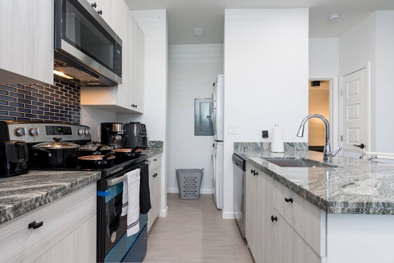 A modern kitchen with white cabinetry, a stainless steel stove, a microwave, and a granite countertop.