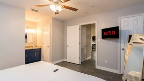 Een slaapkamer met een bed, een plafondventilator, een aan de muur bevestigde televisie en een deur naar een andere kamer.